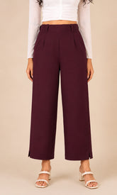 A model wearing mid-rise, wide-leg cropped pants in a deep burgundy color, paired with a white long-sleeve crop top and white heeled sandals, set against a solid beige background.