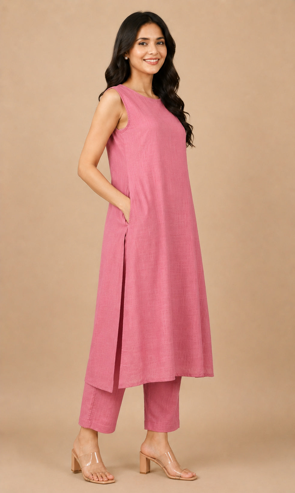 A woman modeling a sleeveless dusty pink cotton kurta with matching trousers, standing against a solid beige studio background.