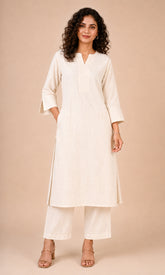 A woman modeling a cream-colored cotton kurta with matching wide-leg trousers, photographed against a solid beige studio background.
