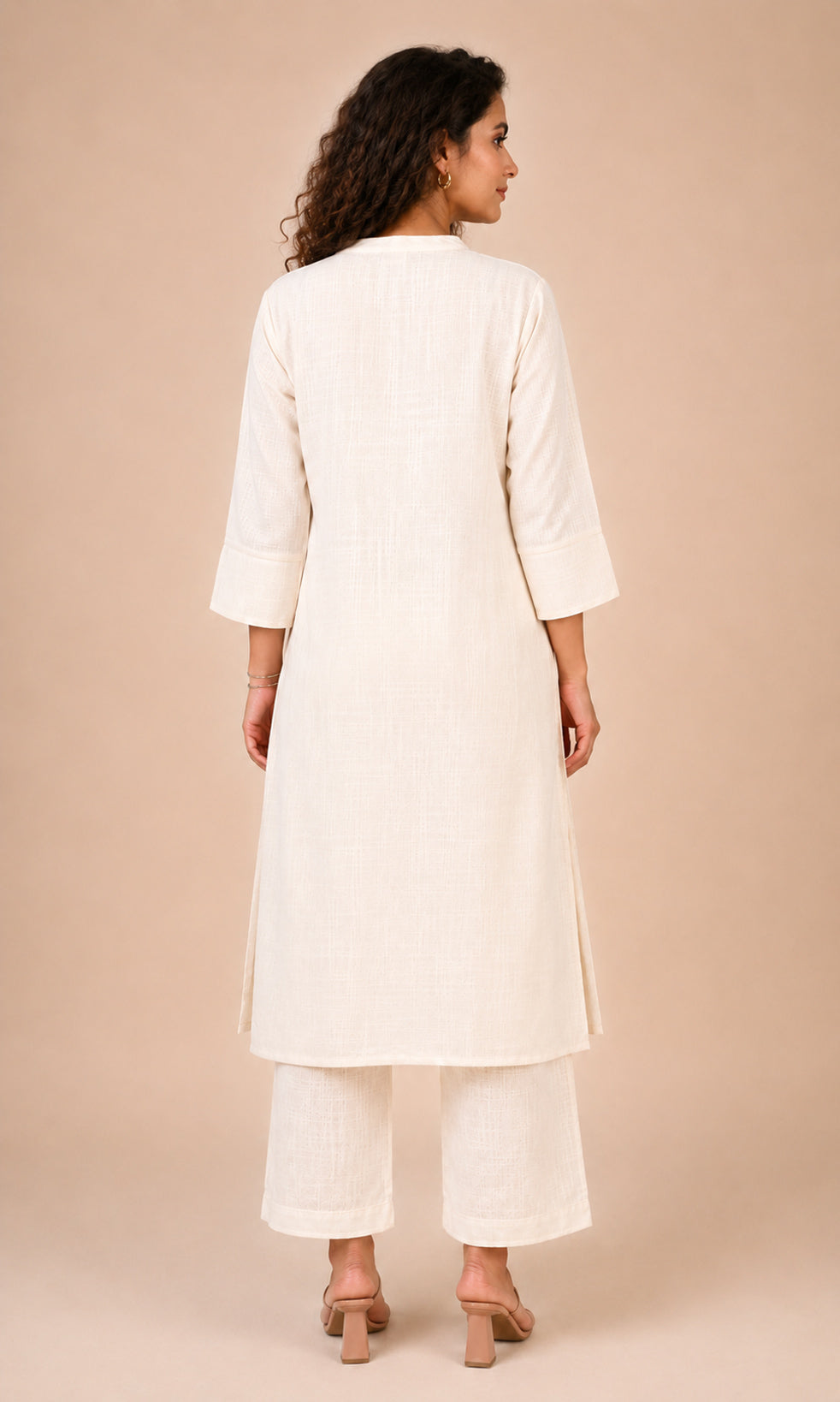 A woman shown from the back wearing a cream-colored kurta and matching wide-leg pants against a solid beige studio background.