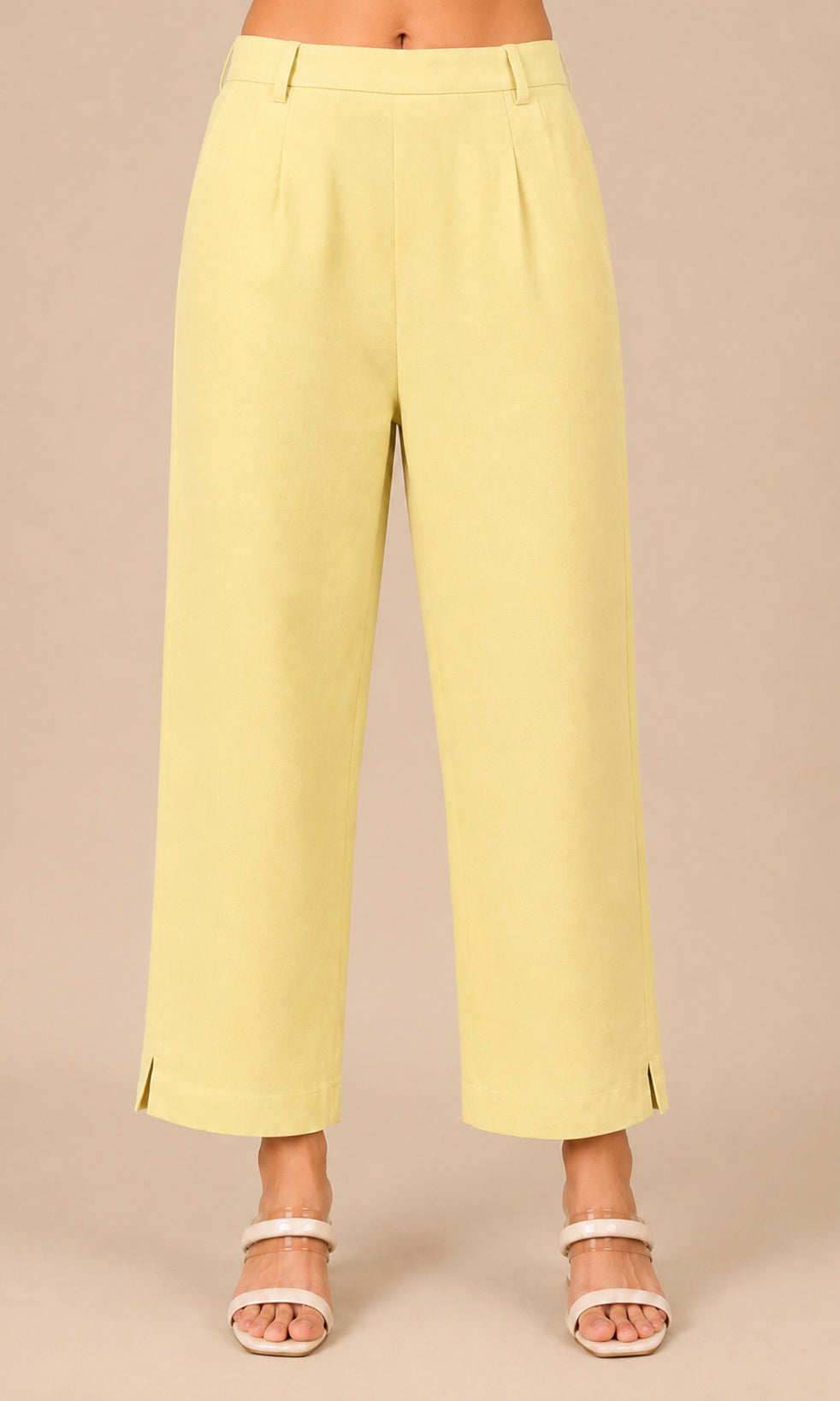 A person wearing pale yellow cropped wide-leg pants with side slits and white heeled sandals, standing against a plain beige studio background.