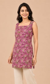 A woman modeling a sleeveless pink kurtaiwith a green and beige floral block print, paired with beige trousers, against a solid beige background.