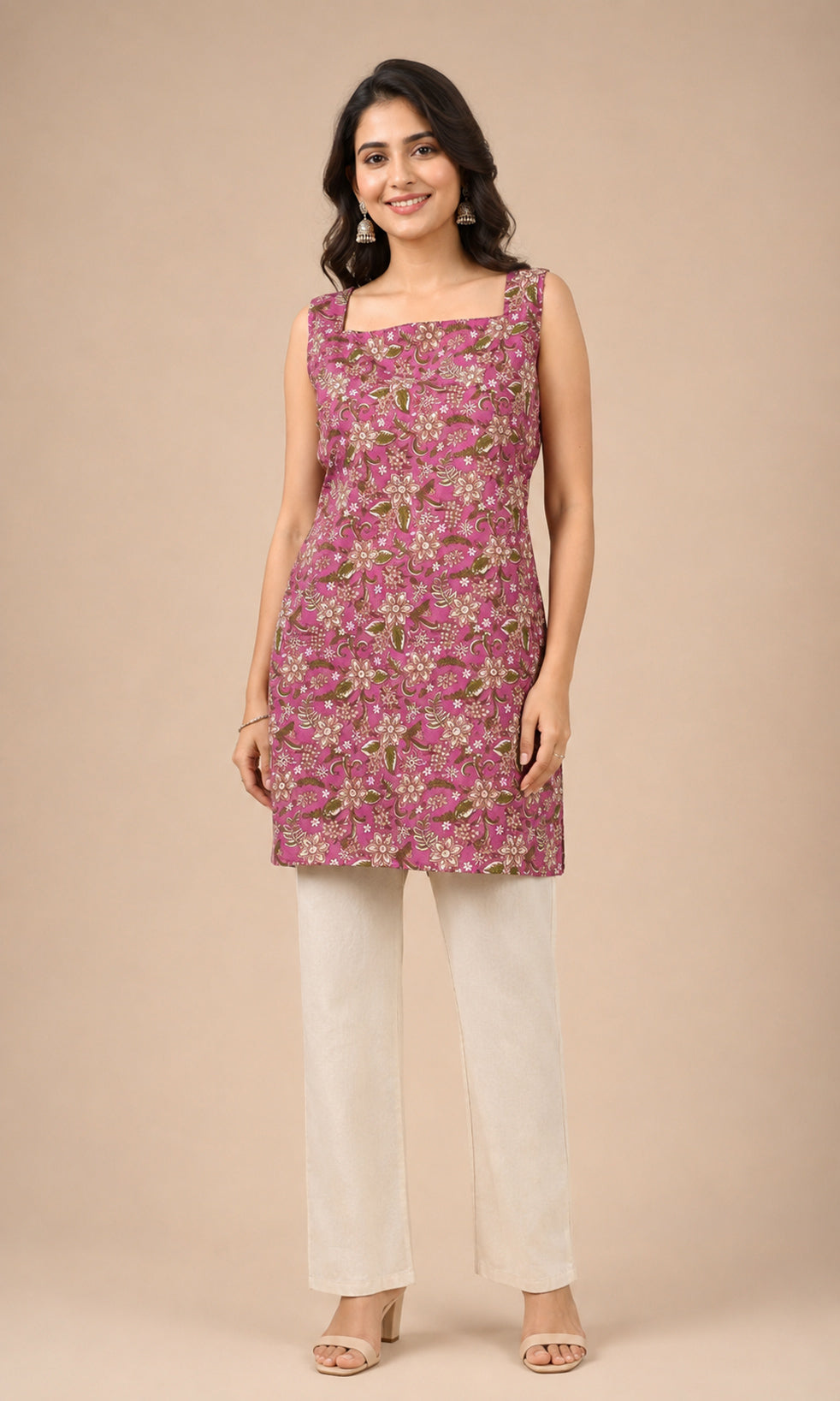 A woman modeling a sleeveless magenta kurti with a green and white floral print, paired with off-white trousers, against a solid beige studio background.