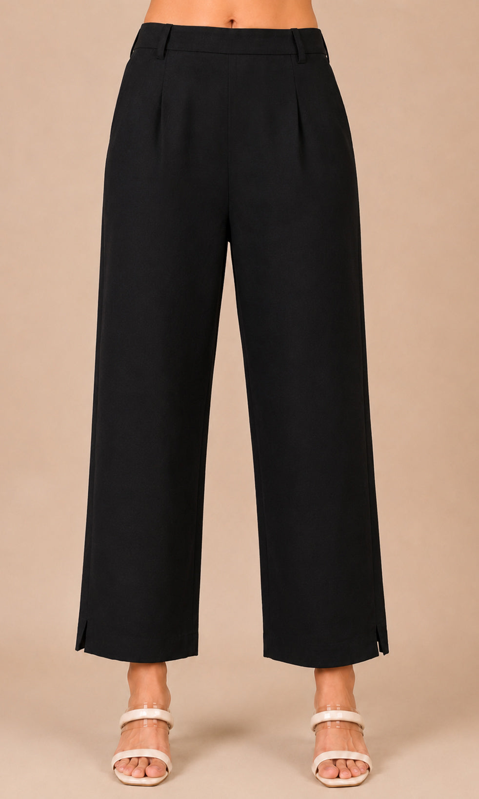 Black wide-leg cropped pants shown on a model from the waist down, paired with white heeled sandals against a solid beige studio background.