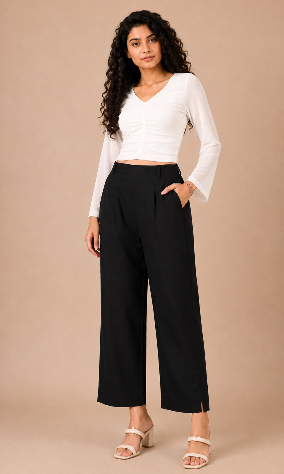 A woman modeling a white long-sleeve cropped top and black wide-leg cropped pants against a solid beige studio background.