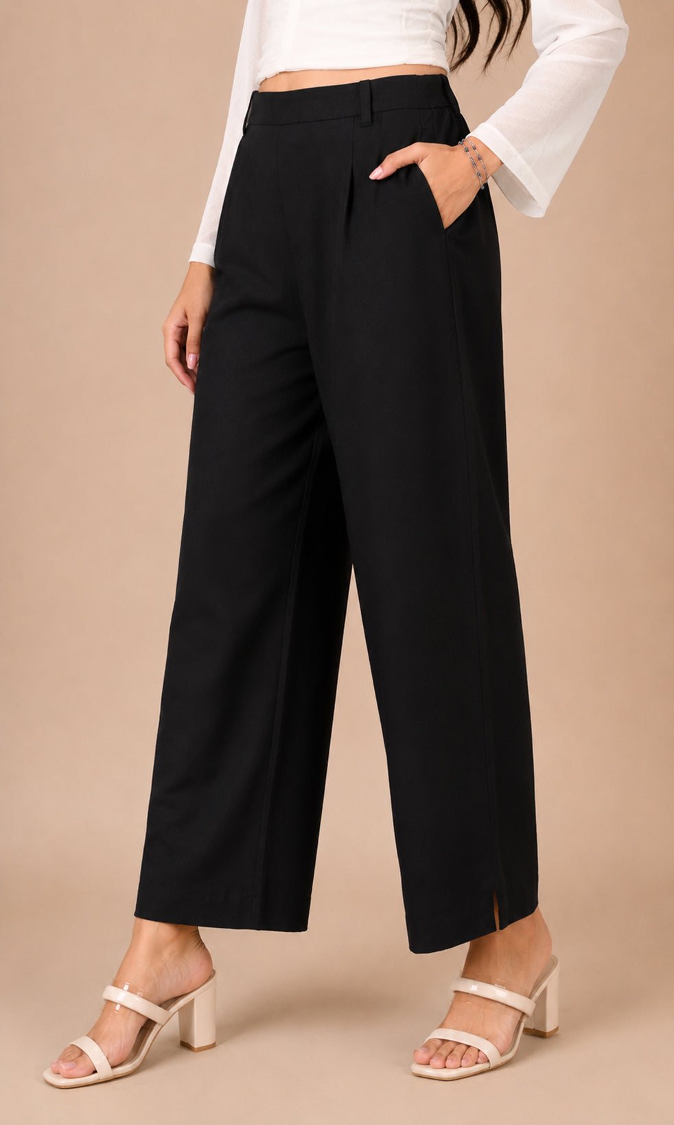 A model wearing black wide-leg cropped pants with side slits, paired with a white long-sleeve crop top and white heeled sandals, standing against a solid beige studio background.