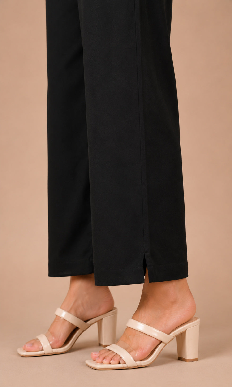 Beige strappy mule sandals with a block heel worn with black cropped trousers, shown on a model against a solid beige background.