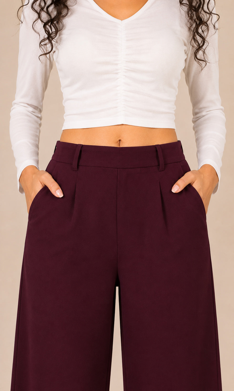 A person wearing high-waisted burgundy wide-leg trousers with pleats and side pockets, paired with a white long-sleeve crop top, shown against a plain beige studio background.
