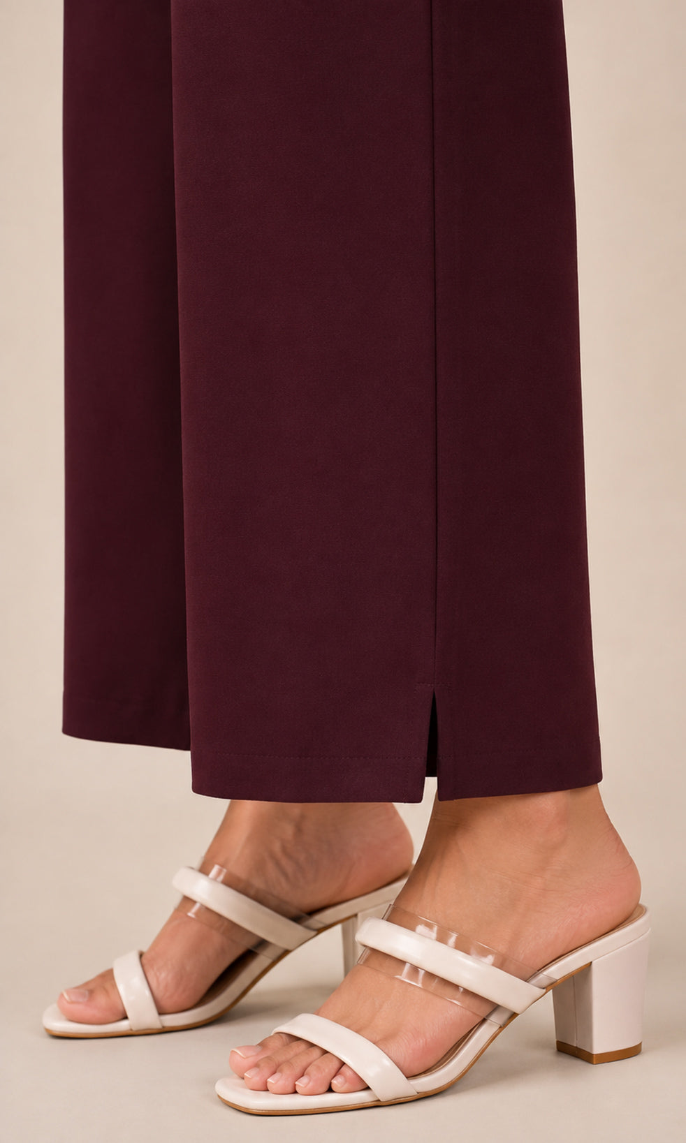 White leather block-heel slide sandals with clear rhinestone straps, shown on a model wearing dark burgundy wide-leg trousers against a light beige background.