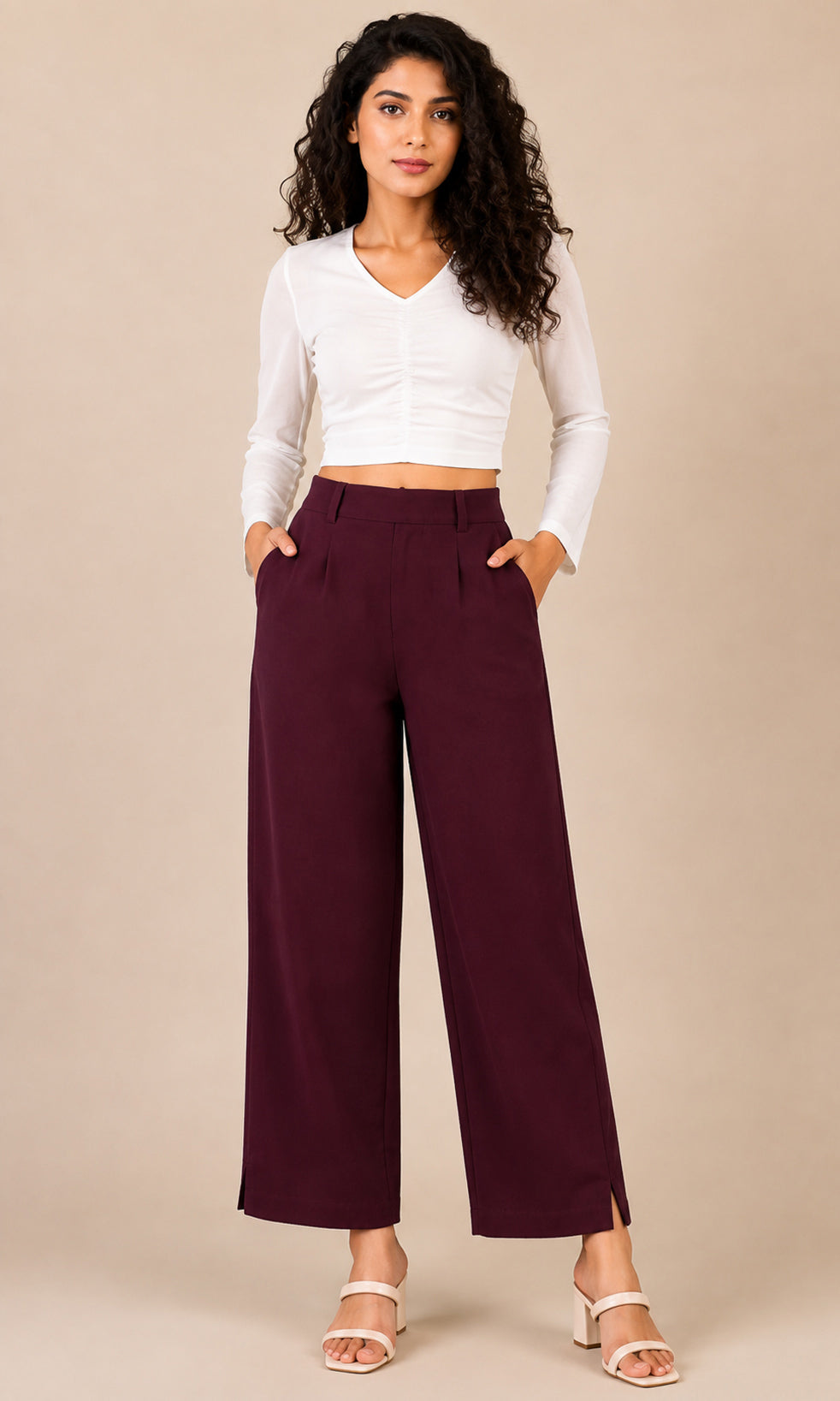 A woman modeling a white long-sleeve cropped top and high-waisted burgundy wide-leg pants against a solid beige studio background.