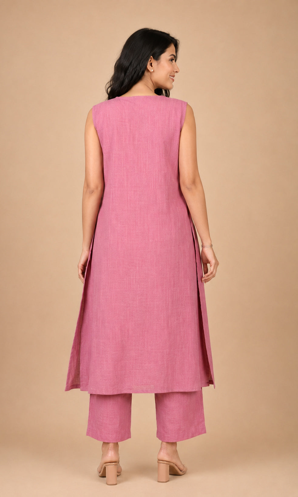 A woman shown from the back wearing a sleeveless dusty pink kurta and matching trousers against a solid beige studio background.