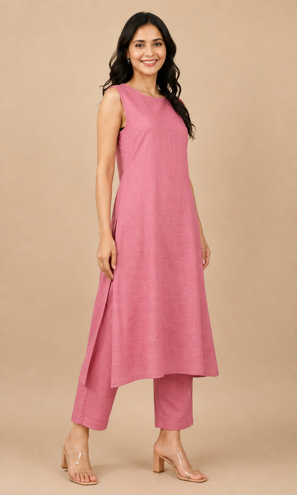 A woman modeling a sleeveless dusty pink kurta with matching cropped pants and clear heeled sandals, standing against a solid beige studio background.