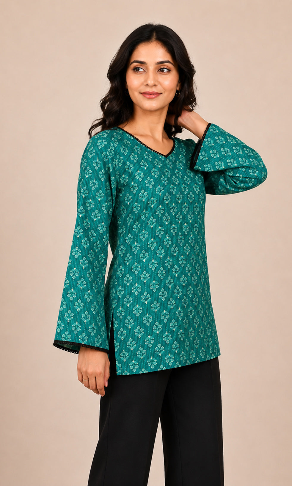 A woman modeling a teal green long-sleeve kurta with a white geometric pattern, paired with black pants, against a solid beige background.
