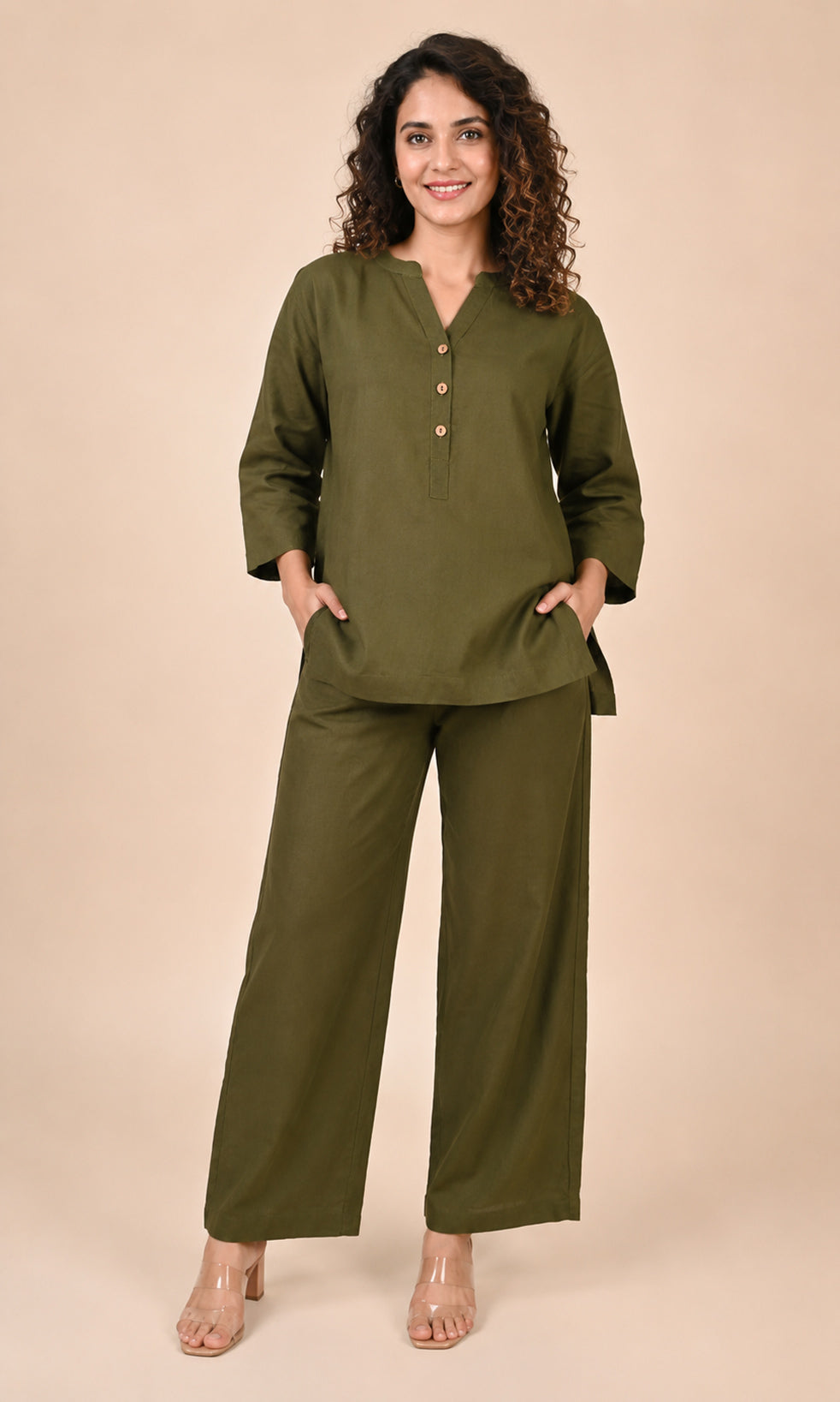 A woman modeling an olive green Co-ord set consisting of a long-sleeve button-up top and matching wide-leg pants, standing against a solid beige studio background.