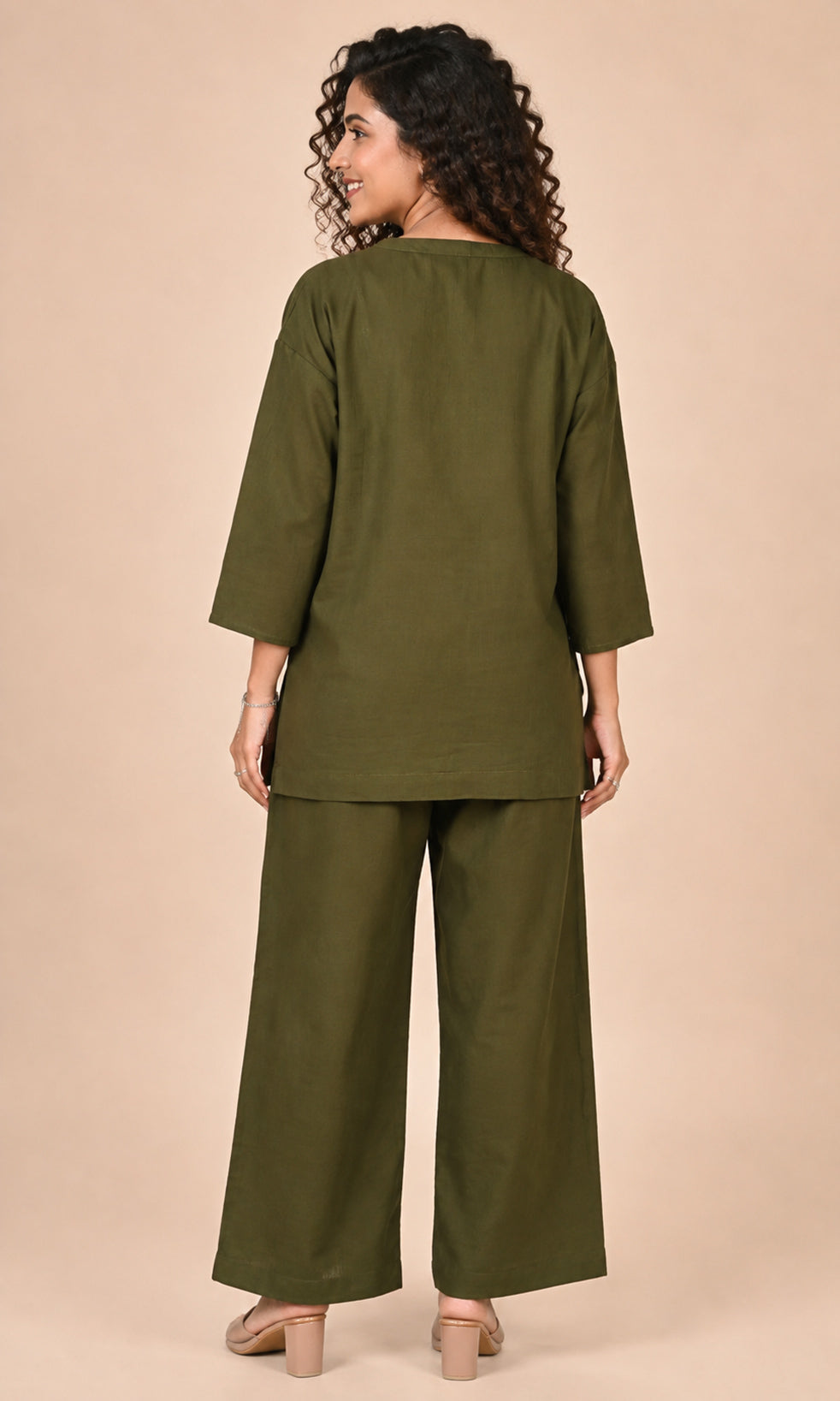 A woman shown from the back wearing an olive green Co-ord set outfit consisting of a loose three-quarter sleeve top and matching wide-leg pants, set against a solid beige studio background.
