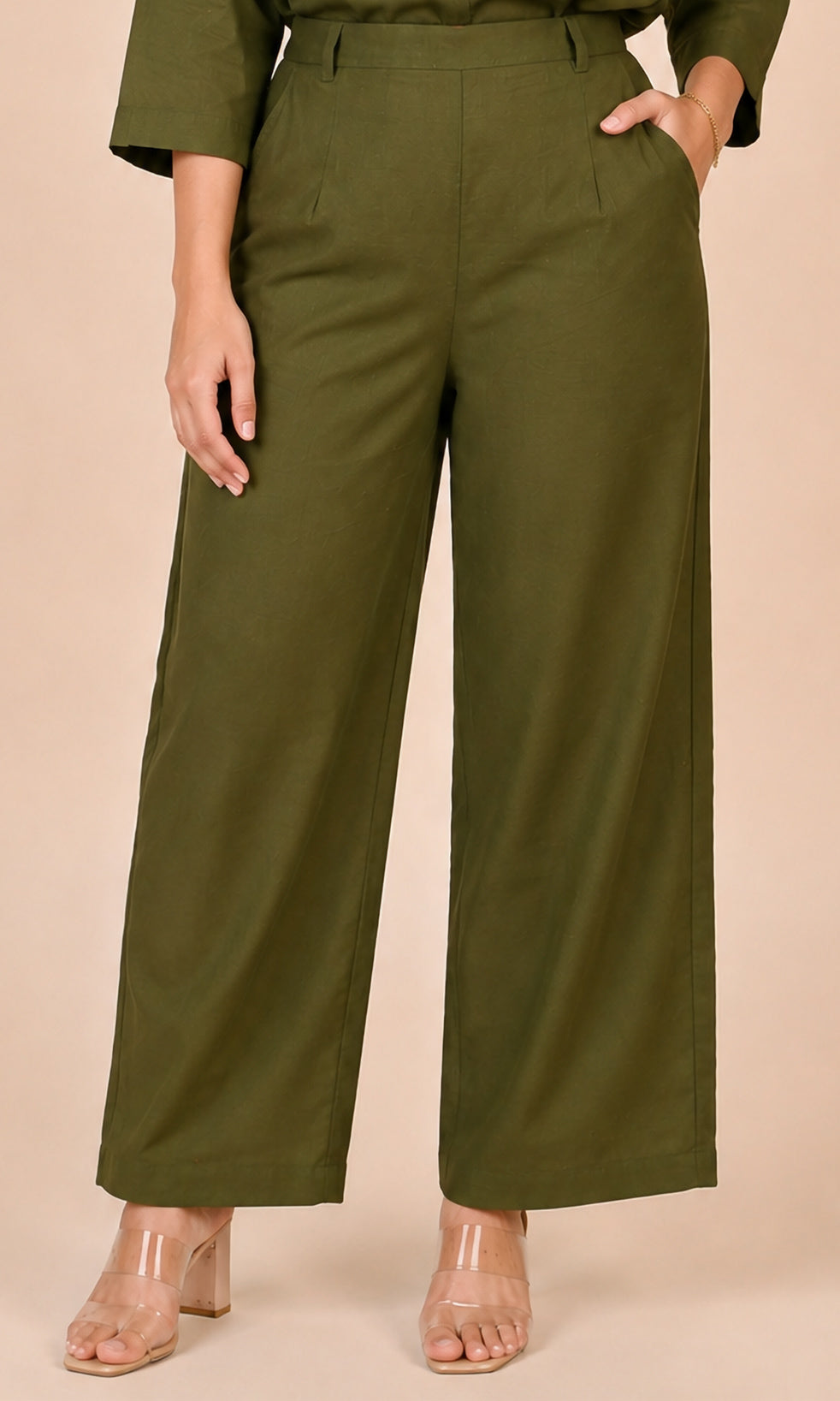 A model wearing olive green wide-leg cropped pants with a matching Co-ord set and clear high-heeled sandals, shown against a solid beige studio background.
