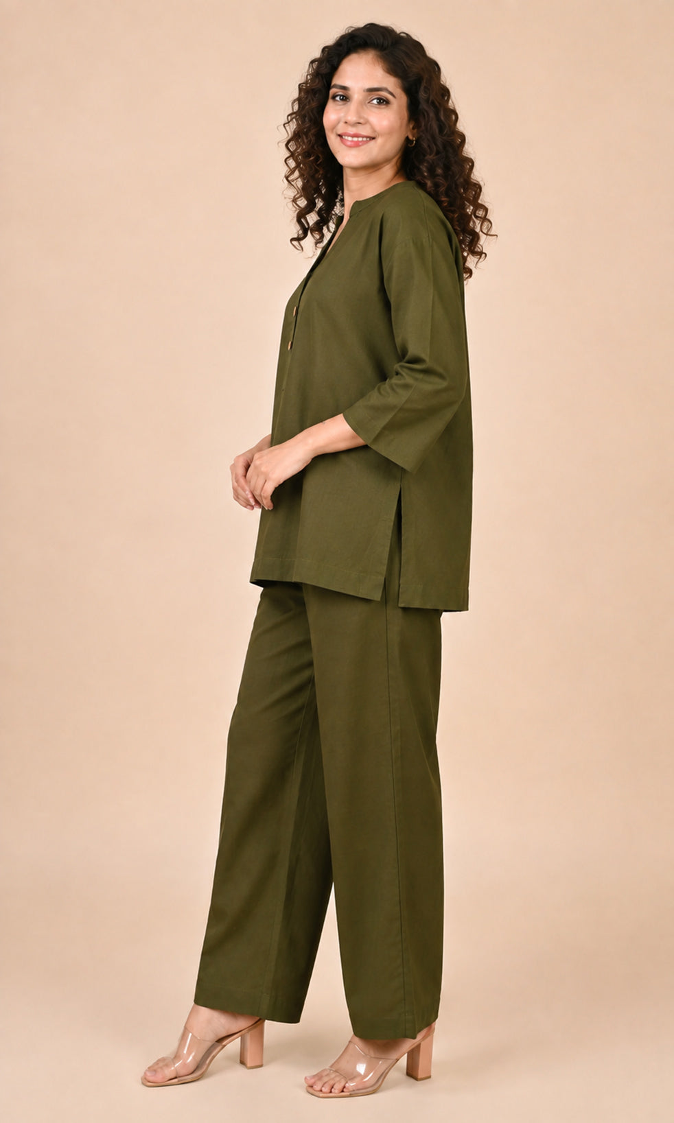 A woman modeling an olive green Co-ord set consisting of a short-sleeve top and matching wide-leg trousers, posed against a solid beige studio background.