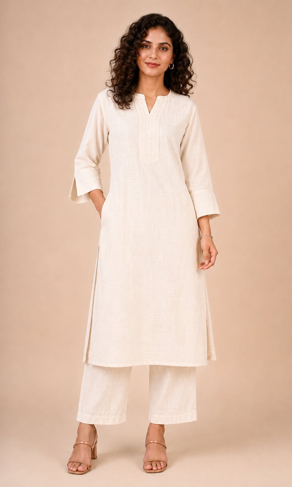 A woman modeling a cream-colored cotton kurta with matching wide-leg trousers, photographed against a solid beige studio background.