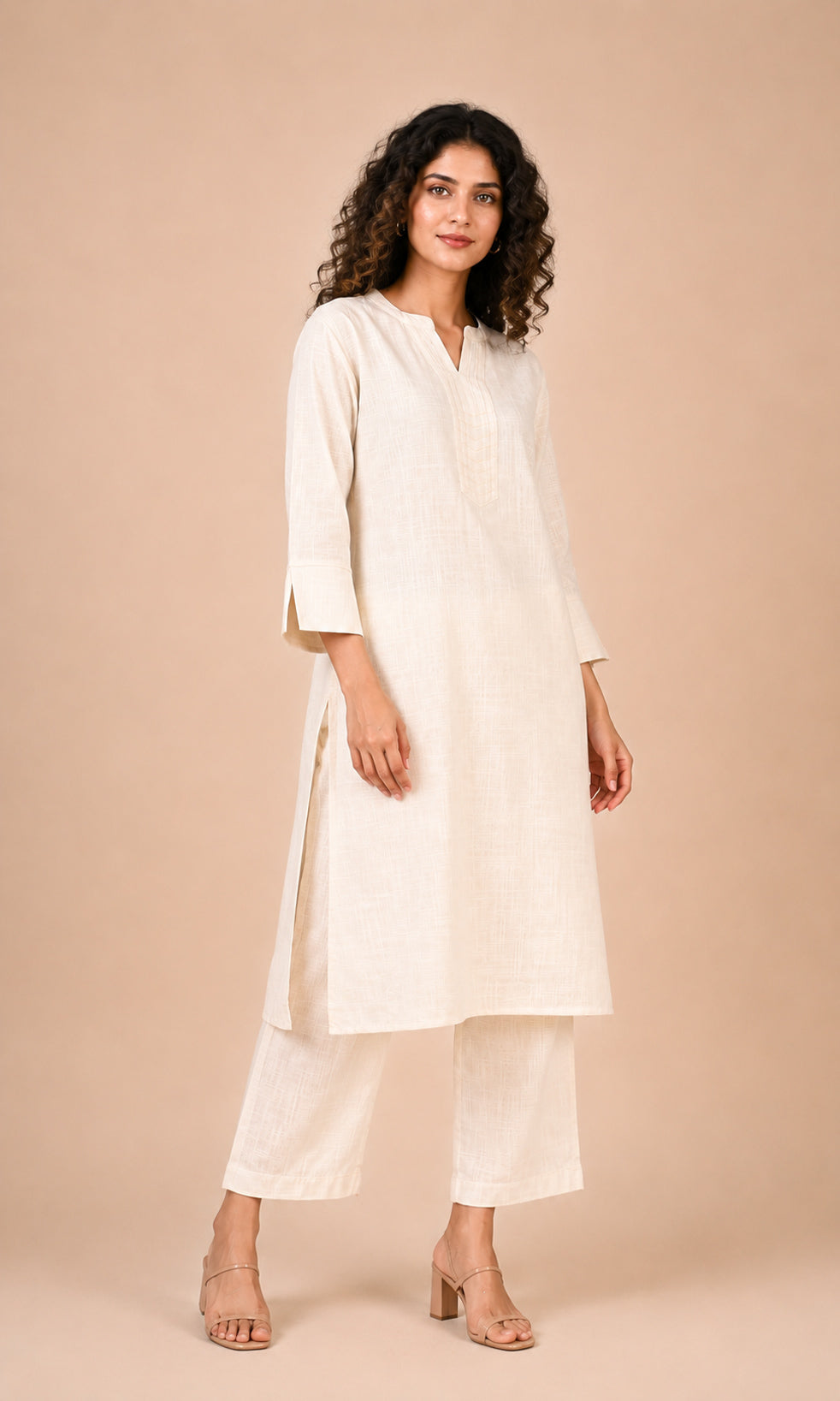 A woman modeling a cream-colored cotton kurta and matching trousers against a solid beige studio background.
