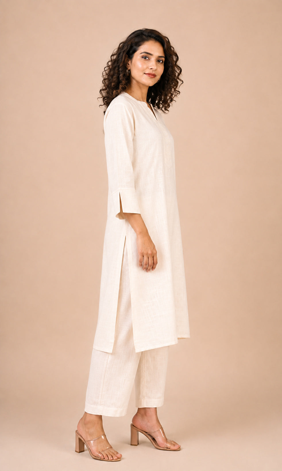 A woman modeling a cream-colored kurta and trouser set against a solid beige studio background.