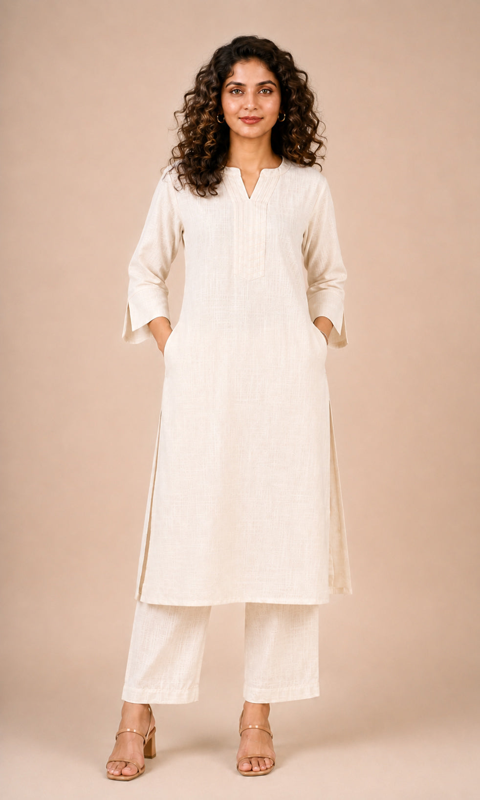 A woman modeling a cream-colored cotton kurta and matching wide-leg trousers against a solid beige studio background.