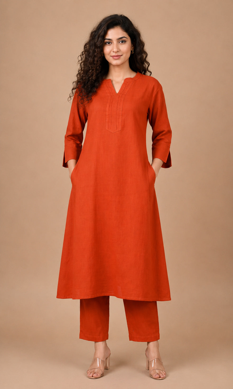 A woman modeling a rust-orange kurta and matching trouser set against a solid beige studio background.