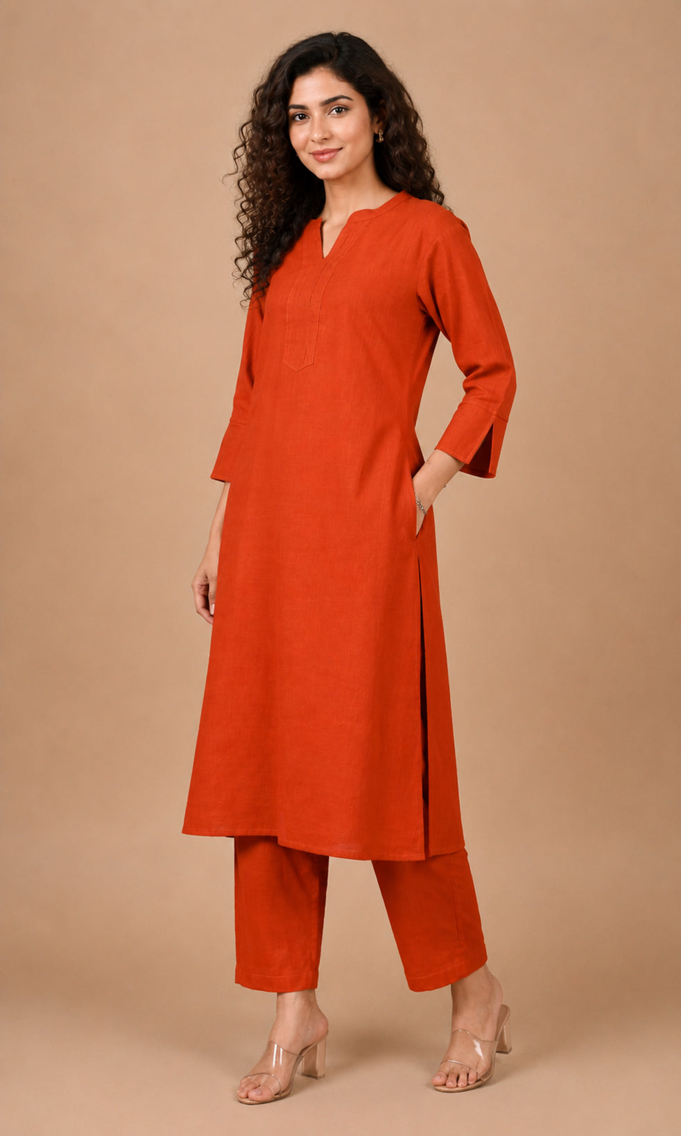 A woman modeling a rust-orange kurta and matching cropped pants against a solid beige studio background.