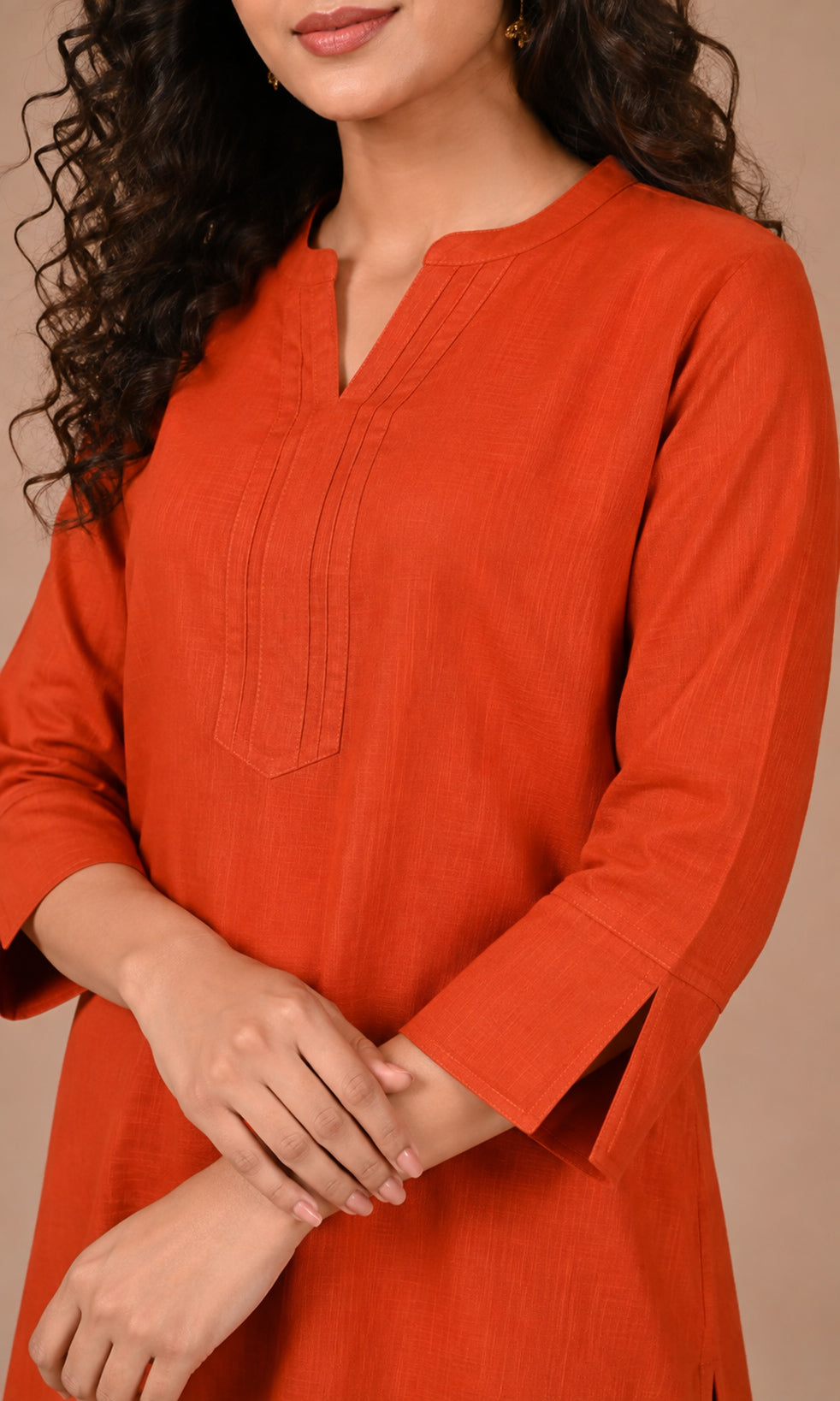 A woman wearing a burnt orange cotton kurta with a split neckline and three-quarter sleeves, shown against a solid beige background.
