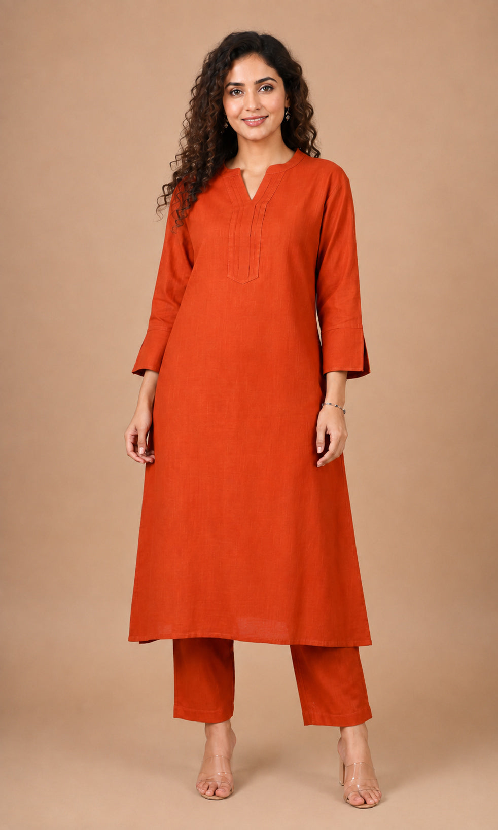 A woman modeling a rust-orange cotton kurta with matching cropped pants against a solid beige studio background.