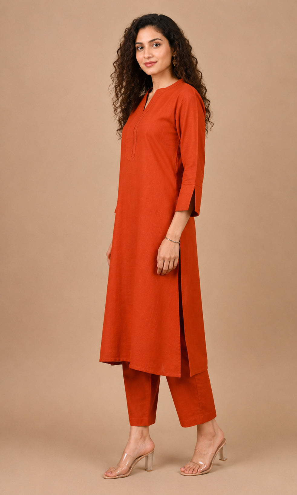 A woman modeling a rust-orange kurta and matching cropped pants against a solid beige studio background.