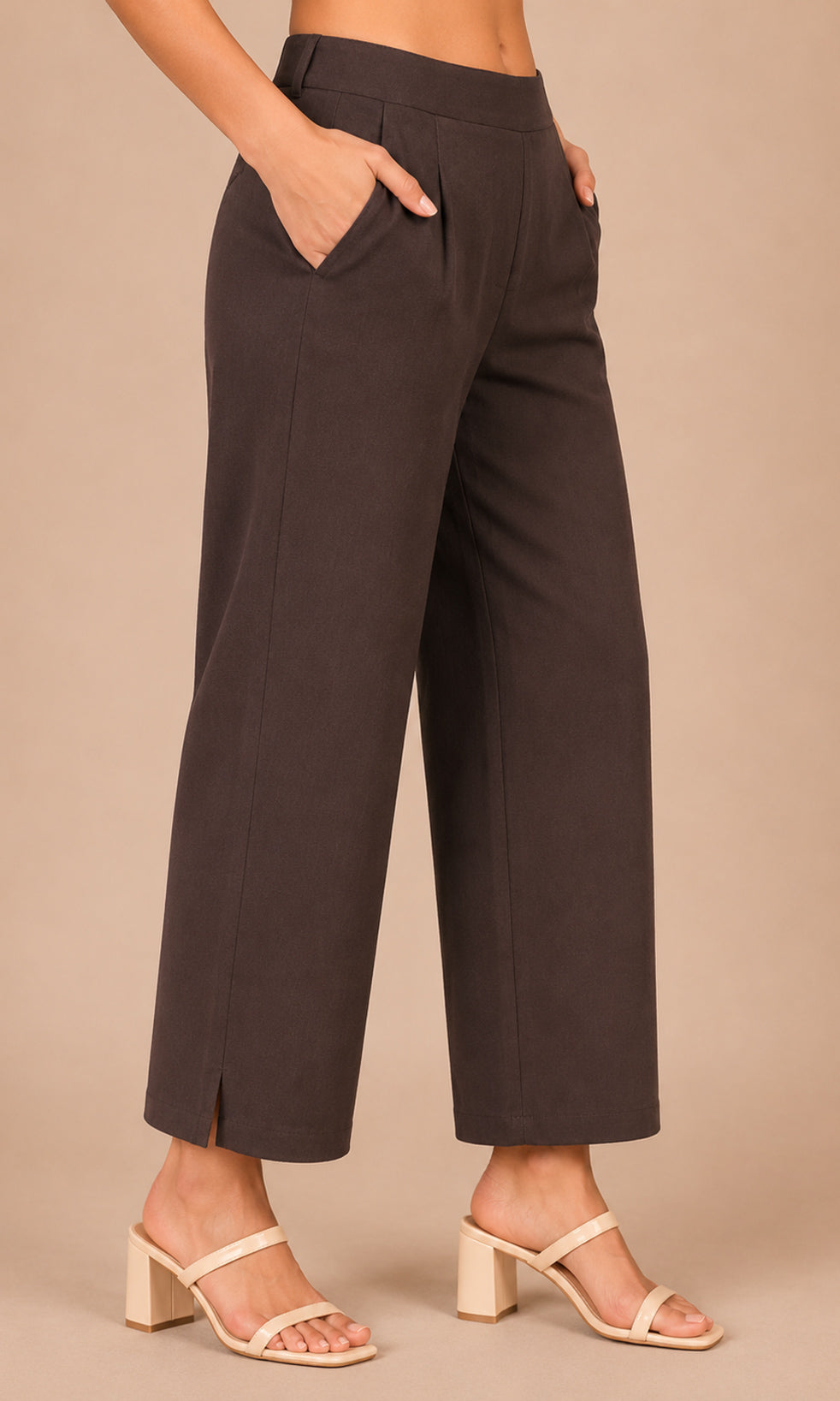 A model wearing dark brown wide-leg cropped pants with side slits and beige block-heel sandals, standing against a solid beige studio background.