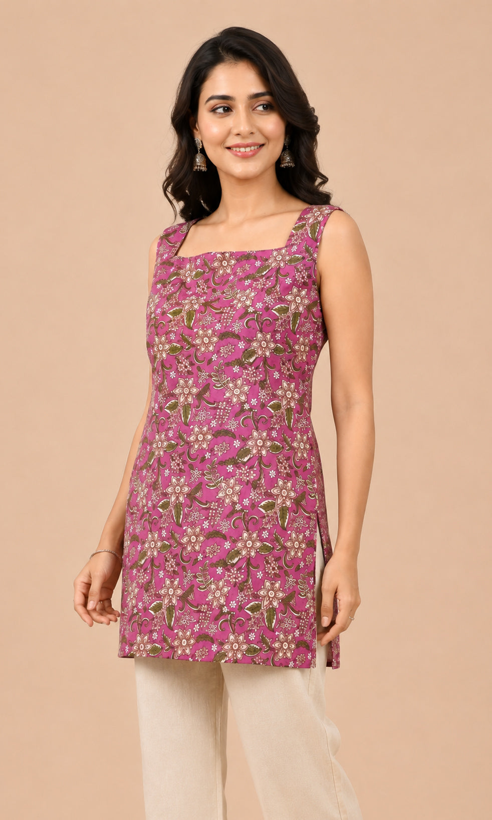 A woman modeling a sleeveless pink kurtaiwith a green and beige floral block print, paired with beige trousers, against a solid beige background.